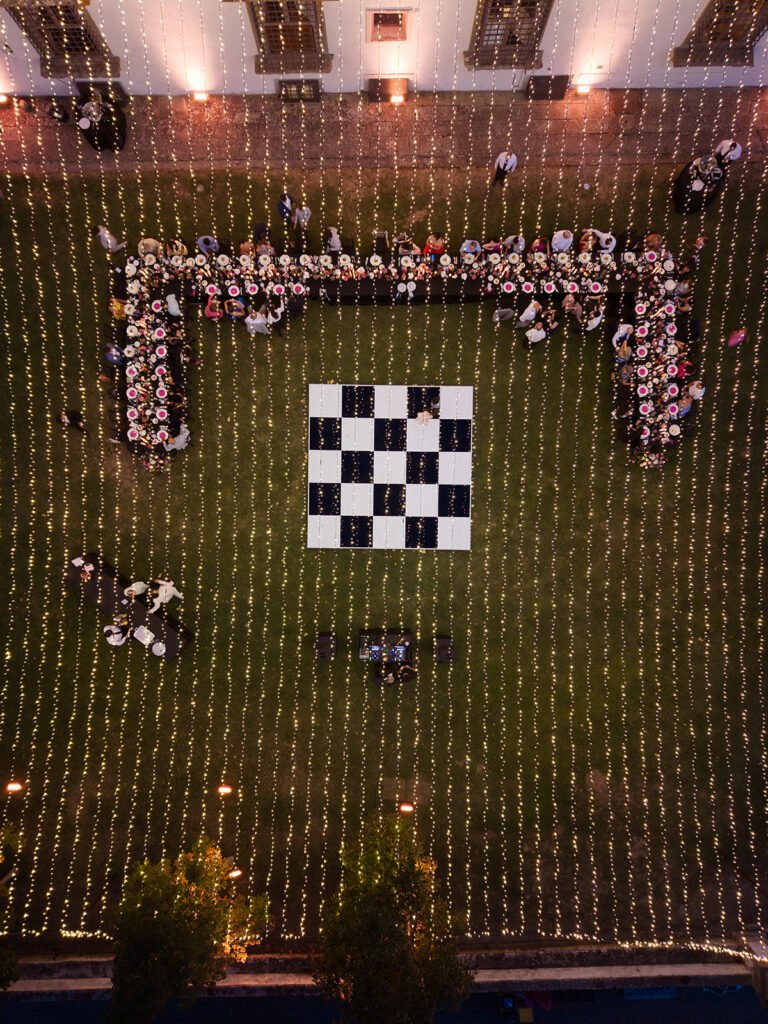 Wedding Dinner from above with fairylight ceiling, black and white checked dancefloor and a U-shape table. The table has black tablecloth and fucsia decor